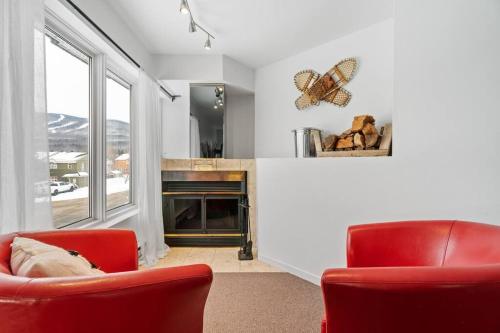 een woonkamer met 2 rode stoelen en een open haard bij INITIAL - LE REPOS DES SKIEURS - Mont-Sainte-Anne in Saint-Férréol-les-Neiges
