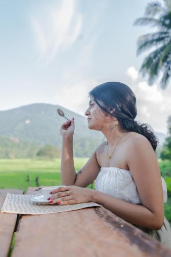 a woman sitting at a table with a spoon in her mouth at Coconut Escapes in Kurunegala