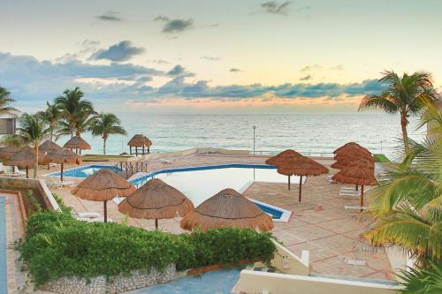 a resort with a swimming pool with umbrellas and the ocean at Brisas Shores Penthouse Beachfront, Ocean View Terrace Cancun Hotel Zone, 2 bedrooms in Cancún