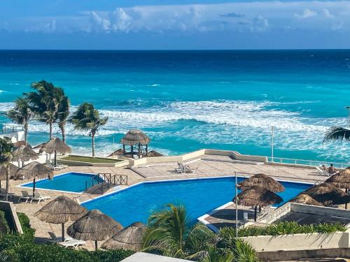 a swimming pool with umbrellas and the ocean at Brisas Shores Penthouse Beachfront, Ocean View Terrace Cancun Hotel Zone, 2 bedrooms in Cancún