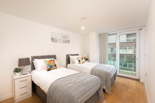 two beds in a white room with a window at Beautiful 2Bed 2Bath Apartment 4Mins to Train Station with WiFi and Free Parking in New Barnet