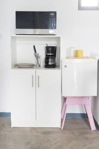 a white kitchen with a microwave and a pink stool at NAPPO Room 2 Alajuela, Heredia,SJO,5min from airport NO PARKING in Guácima