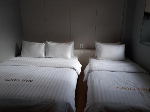 two beds in a room with white sheets and pillows at Grid Inn Hotel in Seoul