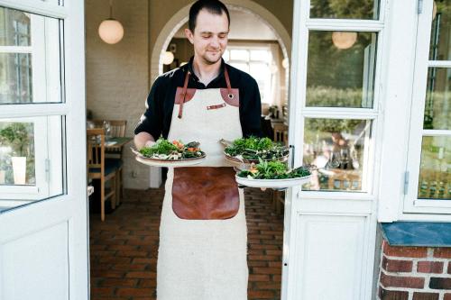 a man in an apron holding two plates of food at Langebjerg Pension & Spisested in Allinge