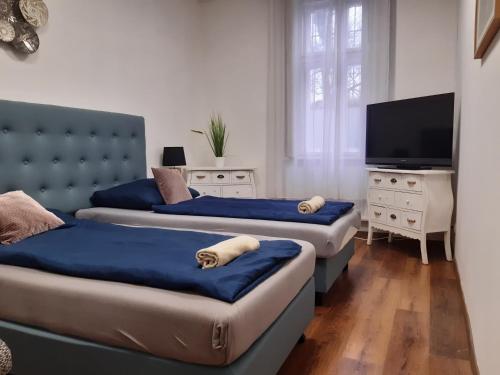 two beds in a room with a tv and a couch at Váralja Apartman in Tata