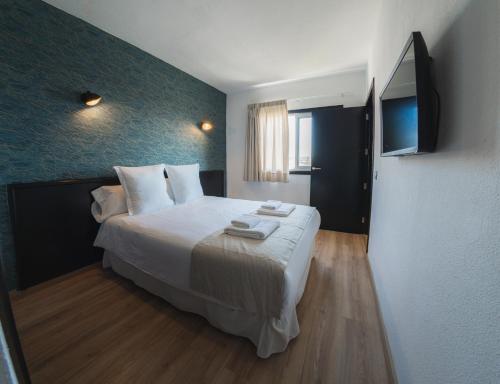una camera da letto con un grande letto con lenzuola bianche e una televisione di Hotel Ventus a El Médano