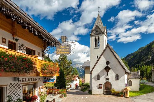 eine kleine weiße Kirche mit einem Kirchturm in einem Dorf in der Unterkunft Alpenhotel La Montanara in Rocca Pietore