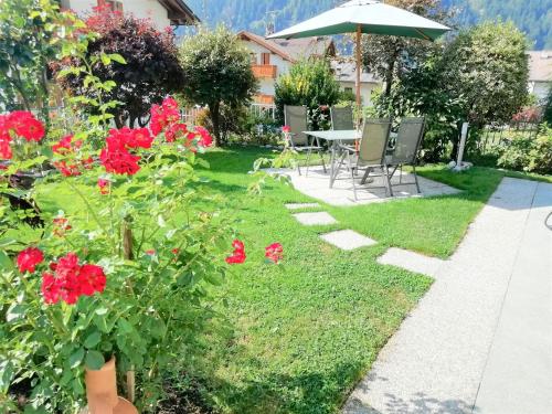 a garden with a table and chairs and red flowers at Appartamento con giardino in Carisolo