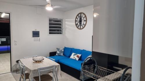 a living room with a blue couch and a clock on a wall at Les hauts du fromager in Le Diamant