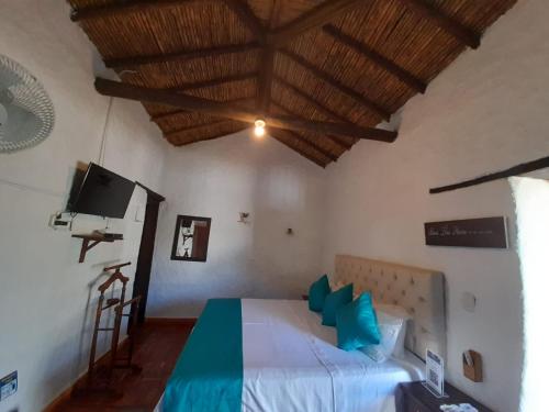 a bedroom with a bed with blue pillows and a tv at Hotel Santos De Piedra - MARANATHA BARICHARA in Barichara