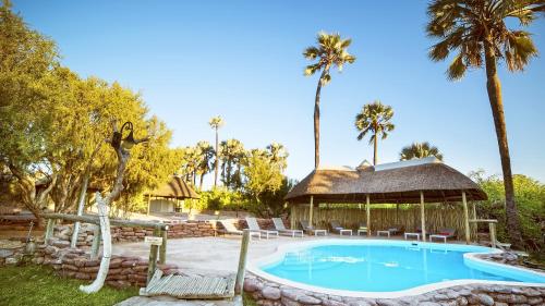 a swimming pool with a gazebo and palm trees at Palmwag Lodge in Palm