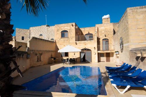 a swimming pool in front of a building with blue chairs at Centre Island Holiday Home with private pool and hot tub in Kerċem
