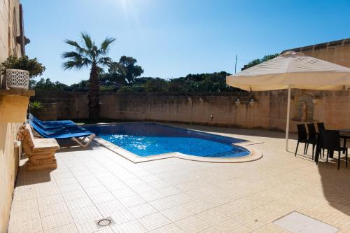 a swimming pool with an umbrella and a table and chairs at Centre Island Holiday Home with private pool and hot tub in Kerċem