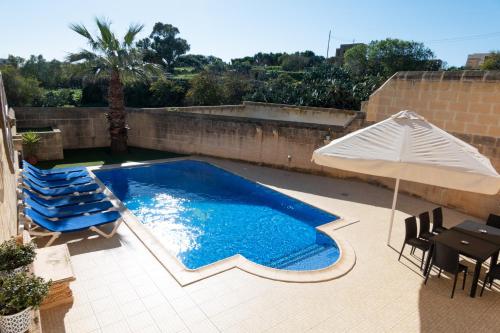 a swimming pool with an umbrella and chairs and a table at Centre Island Holiday Home with private pool and hot tub in Kerċem