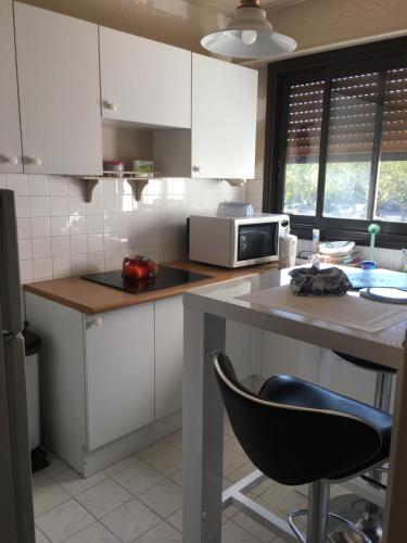 une cuisine avec des armoires blanches et un comptoir avec une chaise noire dans l'établissement Poitiers appartement T2 à 15 mn du Futuroscope, à Poitiers