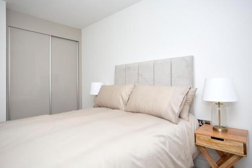 a white bedroom with a bed and a nightstand with a lamp at Luxury Duplex 2-Bed Apartment Fruit Market Marina in Hull