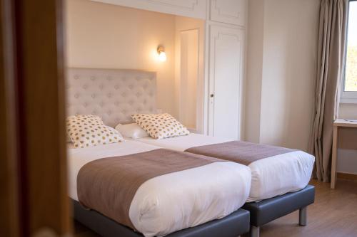two beds in a hotel room with two pillows at The Originals City, Hôtel Mondial, Perpignan in Perpignan