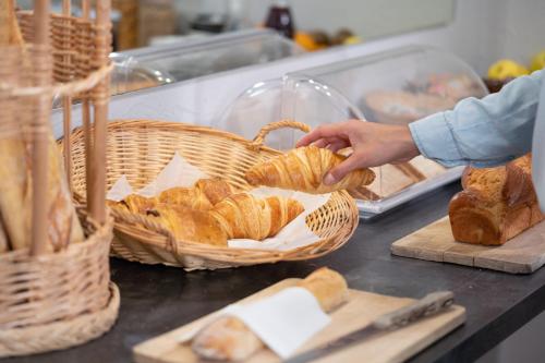 a person reaching for bread in a basket on a counter at The Originals City, Hôtel Mondial, Perpignan in Perpignan