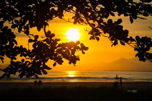 a sunset on the beach with people walking on the beach at Pousada Acqua Bella PISCINA CLIMATIZADA in Bertioga