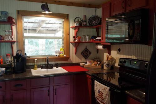 cocina con armarios rojos, fregadero y ventana en Cabin 2 - Modern Cabin Rentals in Southwest Mississippi at Firefly Lane, en Summit