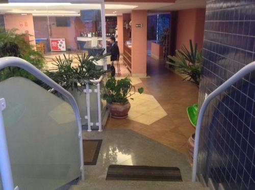 a person walking down a hallway with plants in a building at Hotel Santamaria in Guarujá