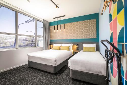 two beds in a room with blue walls and windows at Royal Hotel by Nightcap Social in Melbourne