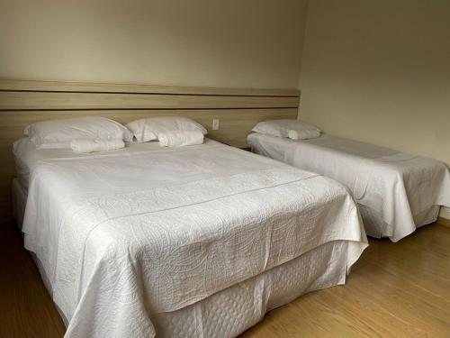 two beds in a hotel room with white sheets at Katuny Pousada e Eventos in São Domingos do Prata