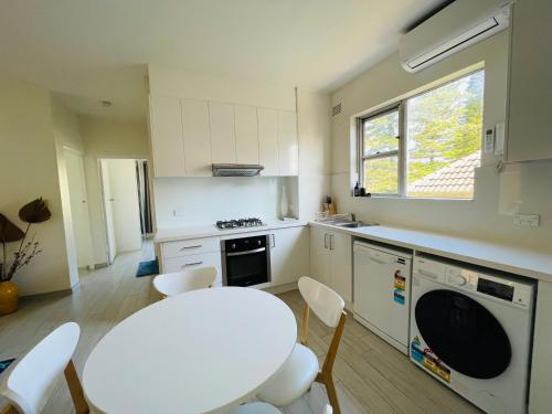 a white kitchen with a white table and chairs at Lotus Stay Manly - Apartment 29A in Sydney