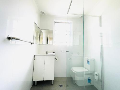 baño blanco con aseo y ducha acristalada en Lotus Stay Manly - Apartment 29A, en Sídney