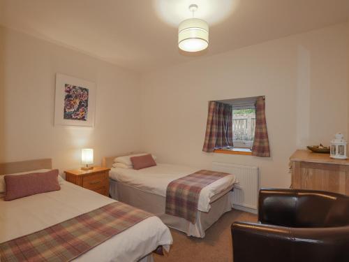 a room with two beds and a chair and a window at Lilac Cottage in Strathpeffer