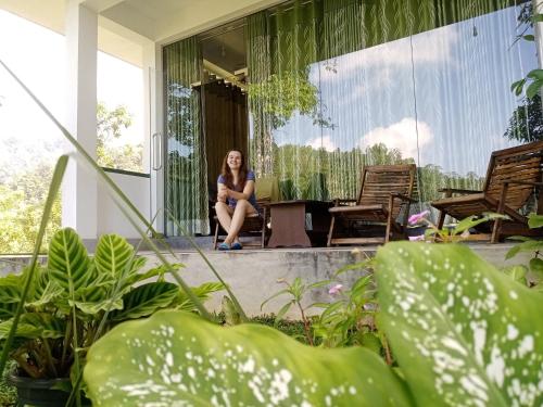 Eine Frau, die auf der Veranda eines Hauses sitzt. in der Unterkunft Evergreen Villa - Sinharaja in Deniyaya