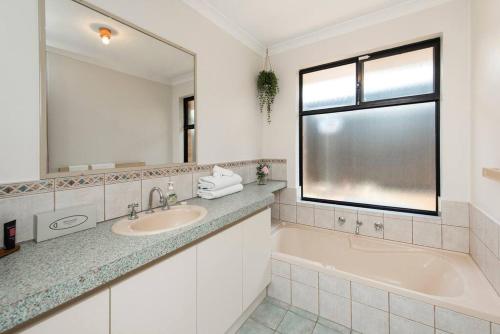 La salle de bains est pourvue d'une baignoire, d'un lavabo et d'un miroir. dans l'établissement Scarborough Villa on Duke - EXECUTIVE ESCAPES, à Perth