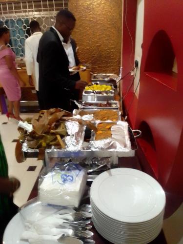 a table with plates of food and a man standing in a room at Royal Park Hotel in Jinja