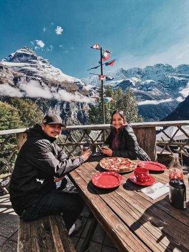 a man and woman sitting at a picnic table with pizza at Mountain Hostel Gimmelwald in Gimmelwald