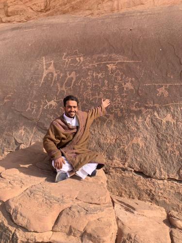a man sitting on some rocks next to a rock wall at Wadi Rum Moon Light Camp in Wadi Rum