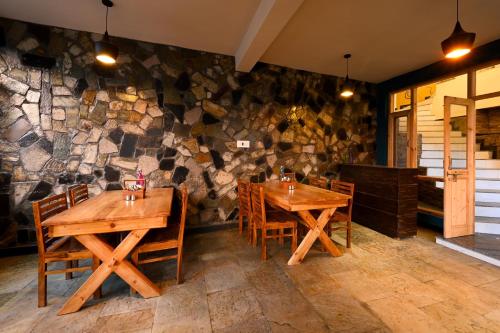 a restaurant with wooden tables and chairs and a stone wall at Zostel Dobhi, Manali in Nagar