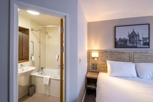 Two Rivers Lodge by Marston’s Inns في تشيبستو: غرفة نوم بسرير وحوض استحمام ومغسلة