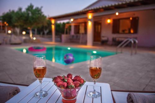 a table with two glasses of wine and a bowl of strawberries at Villa Avra - With Private Pool in Melidhónion