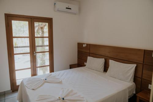 a bedroom with a white bed with a wooden headboard and a window at Pousada Ilha Vitoria in Ubatuba