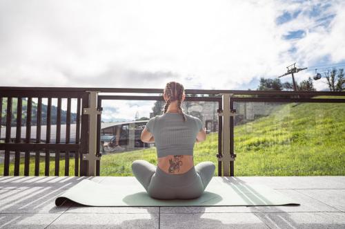 a woman sitting on a yoga mat looking out the window at APART HERZOG - URBAN LUXURY LIFESTYLE direct at Steinbergpiste and Steinbergbahn in Leogang