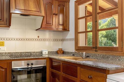 cocina con armarios de madera, fregadero y ventana en Villa Panada, en Pollensa