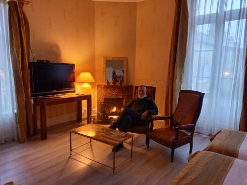 a man sitting in a chair in a living room with a fireplace at Le Belvedere des Remparts in Langres