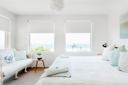 a white bedroom with two beds and two windows at The Ley @ The Sea in Kalk Bay