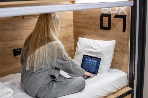 a woman sitting on a bed with a laptop at VIA Hostel in Kazan