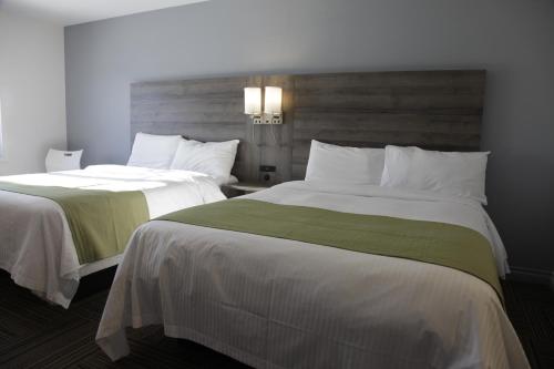 two beds in a hotel room with white and green sheets at Hôtel Énergie Shawinigan in Shawinigan