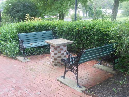 a green park bench and a table on a brick path at Century Suites Hotel in Bloomington