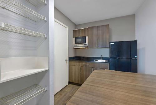 a kitchen with a black refrigerator and wooden cabinets at Studio 6-North Richland Hills, TX - Fort Worth in North Richland Hills