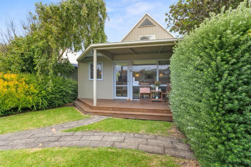 a small house with a wooden porch with a table at Apollo Bay Beach Hut ~ Wifi ~ Opposite The Ocean in Apollo Bay