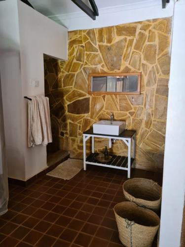baño con pared de piedra y lavamanos en Honey Badger Lodge, en Moshi