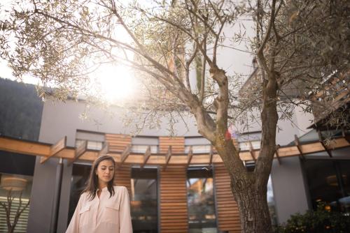 a woman standing next to a tree in front of a building at ALPIANA - green luxury Dolce Vita Hotel in Vollan